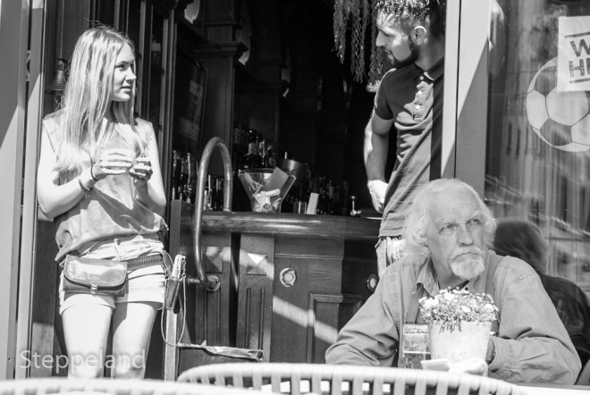 Amsterdam street photography - two young people at a café terrace talking behind the back of an elderly man